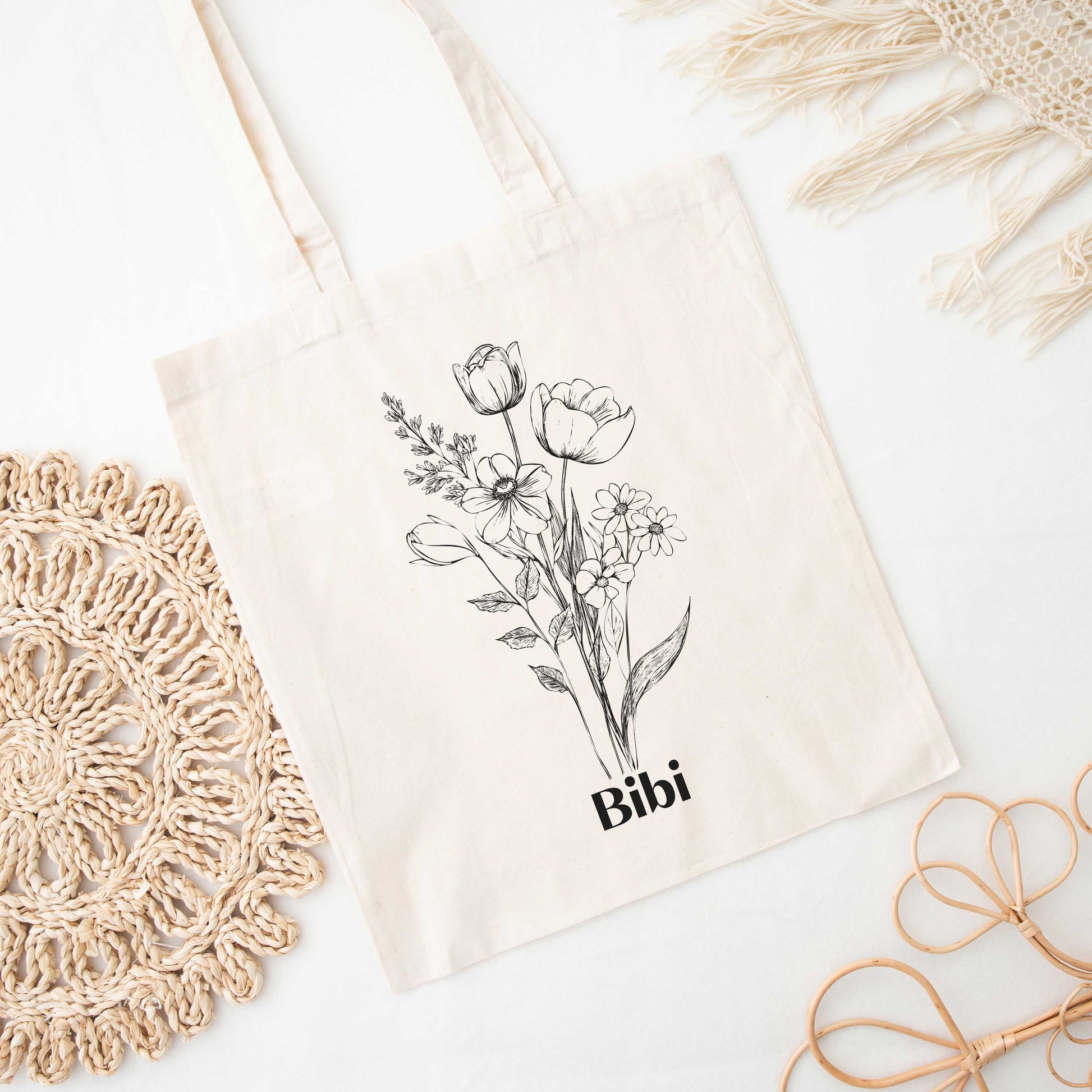 Totebag met zwarte bloemenlijnillustratie en naam Bibi, liggend plat op een witte ondergrond met zachte schaduwen