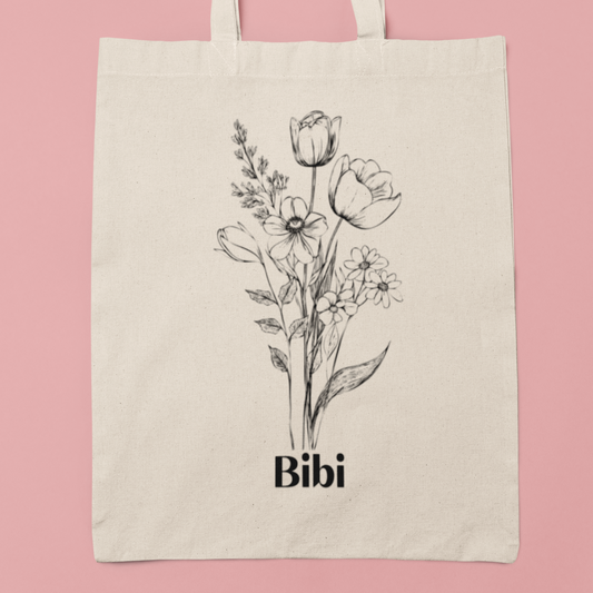 Katoenen totebag op roze achtergrond met zwarte lijntekening van bloemen en daaronder de naam Bibi