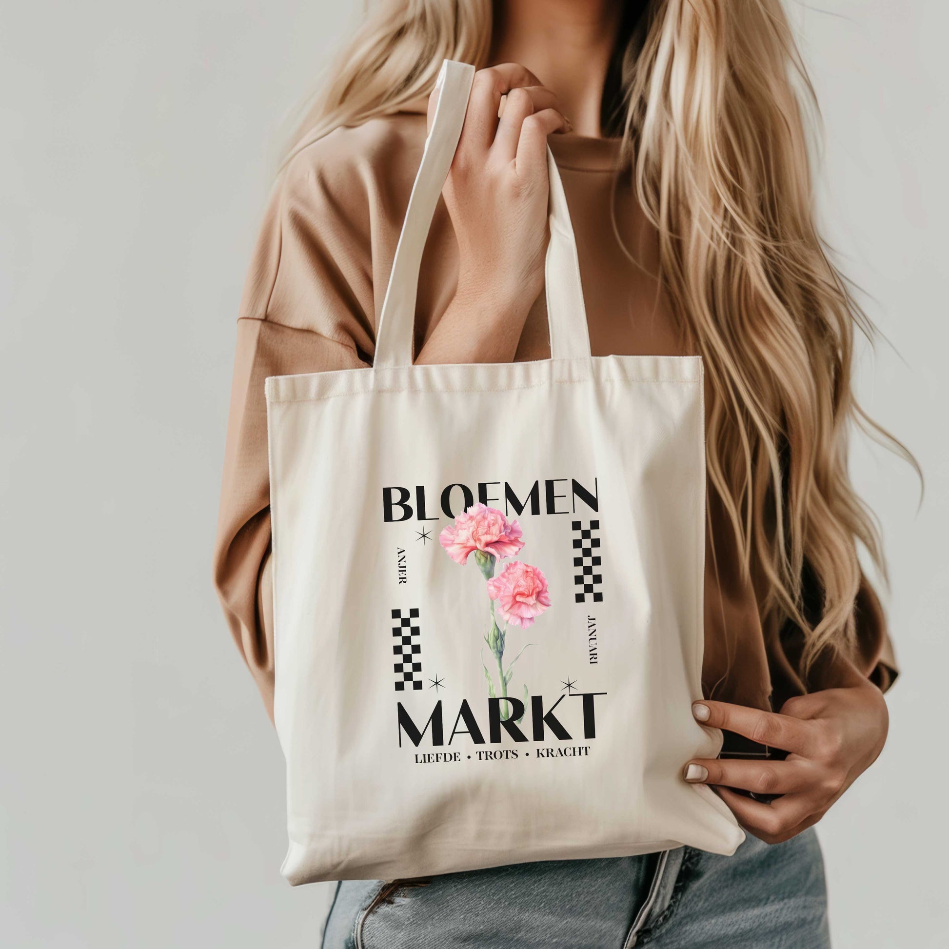 een blonde vrouw die een totebag met de tekst bloemenmarkt met geboortebloem voor de maand januari , een roze aster en de kernwoorden voor deze maand : liefde, trots en kracht , vasthoudt