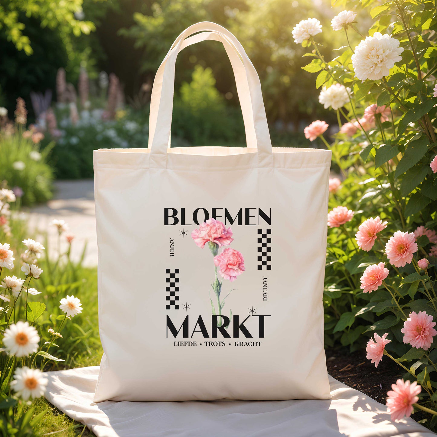 totebag met de tekst bloemenmarkt met geboortebloem voor de maand januari , een roze aster en de kernwoorden voor deze maand : liefde, trots en kracht buiten in een tuin met bloemen