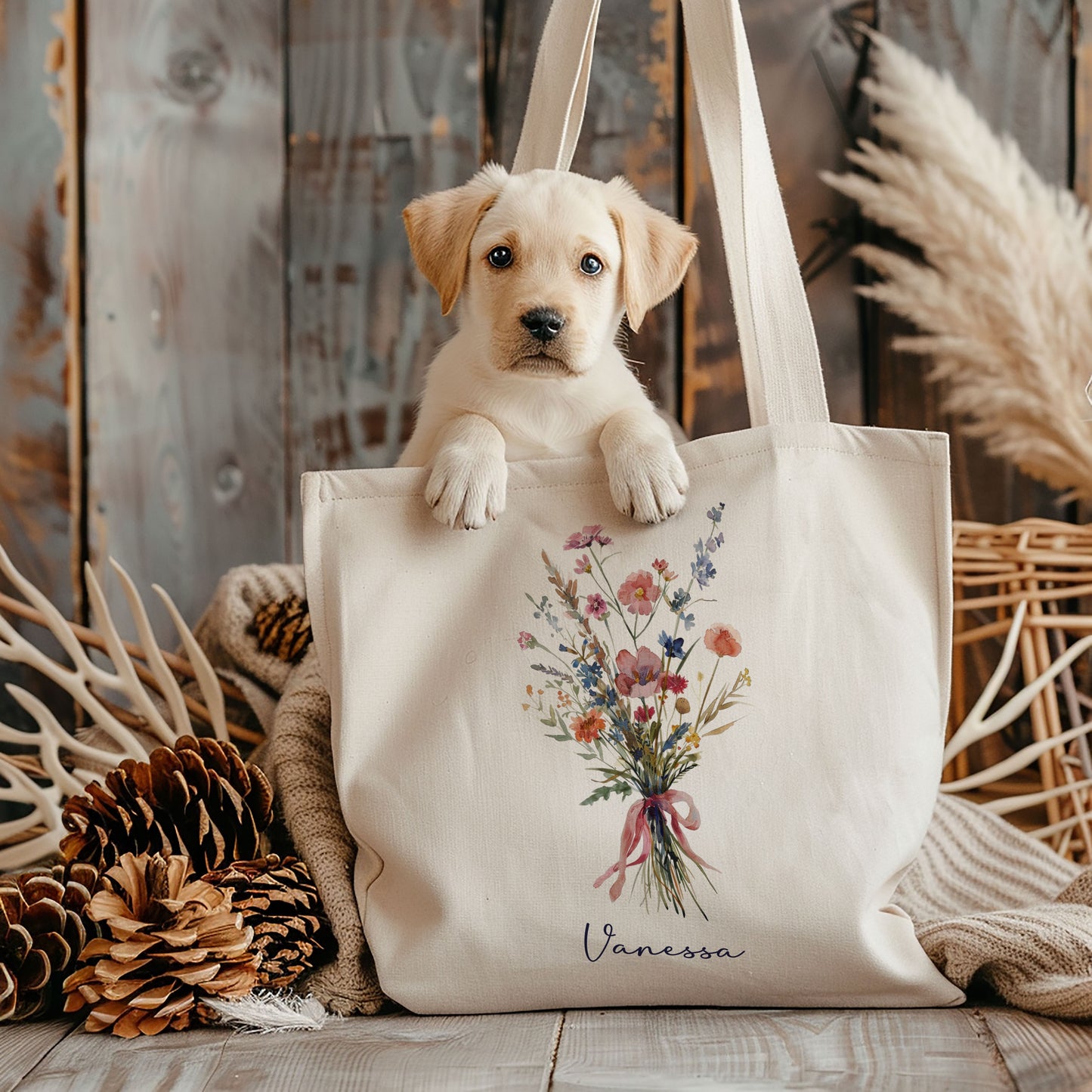 Katoenen totebag met kleurrijk watercolor bloemenboeket en naam, rechtopstaand op de vloer met een puppy erin