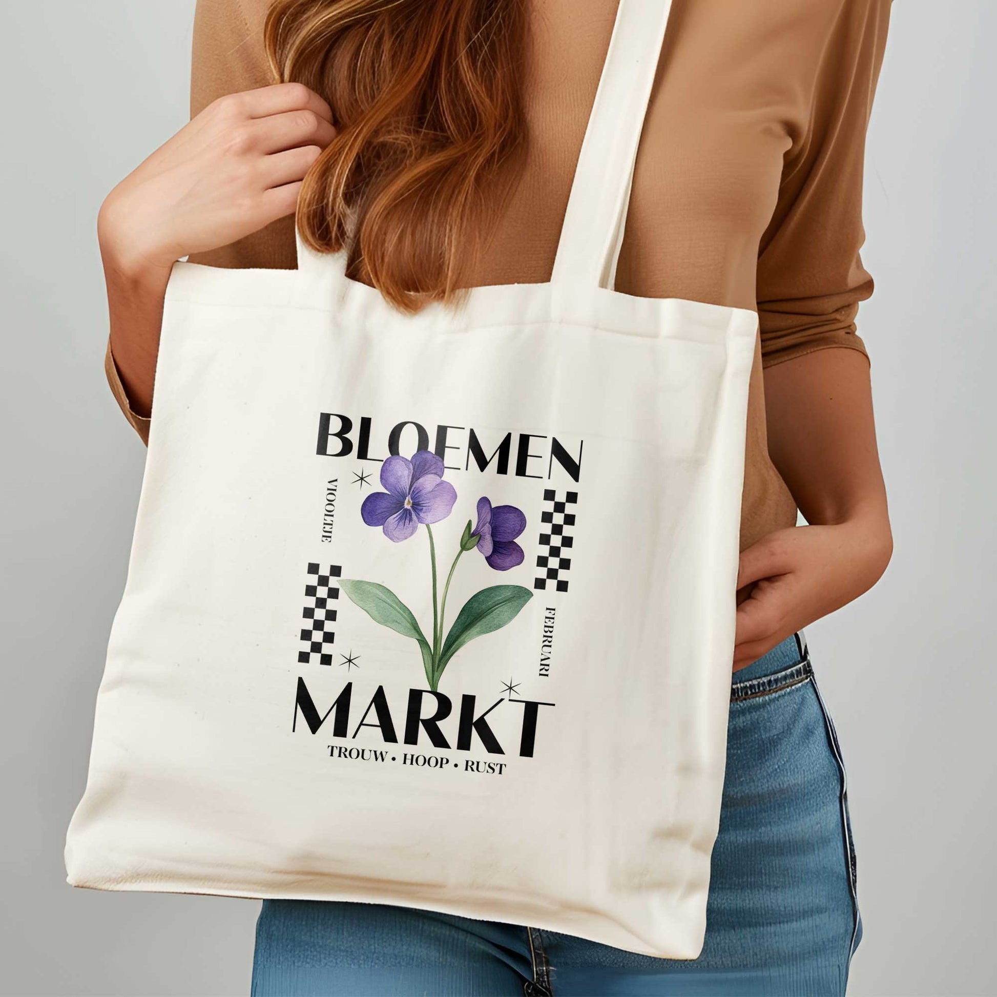 vrouw met rood haar die een totebag om haar hals heeft , totebag met  de tekst bloemenmarkt en een illustratie van een geboortebloem van de maand februari, een viooltje. Met onderaan de kernwoorden van deze maand : trouw, hoop, rust