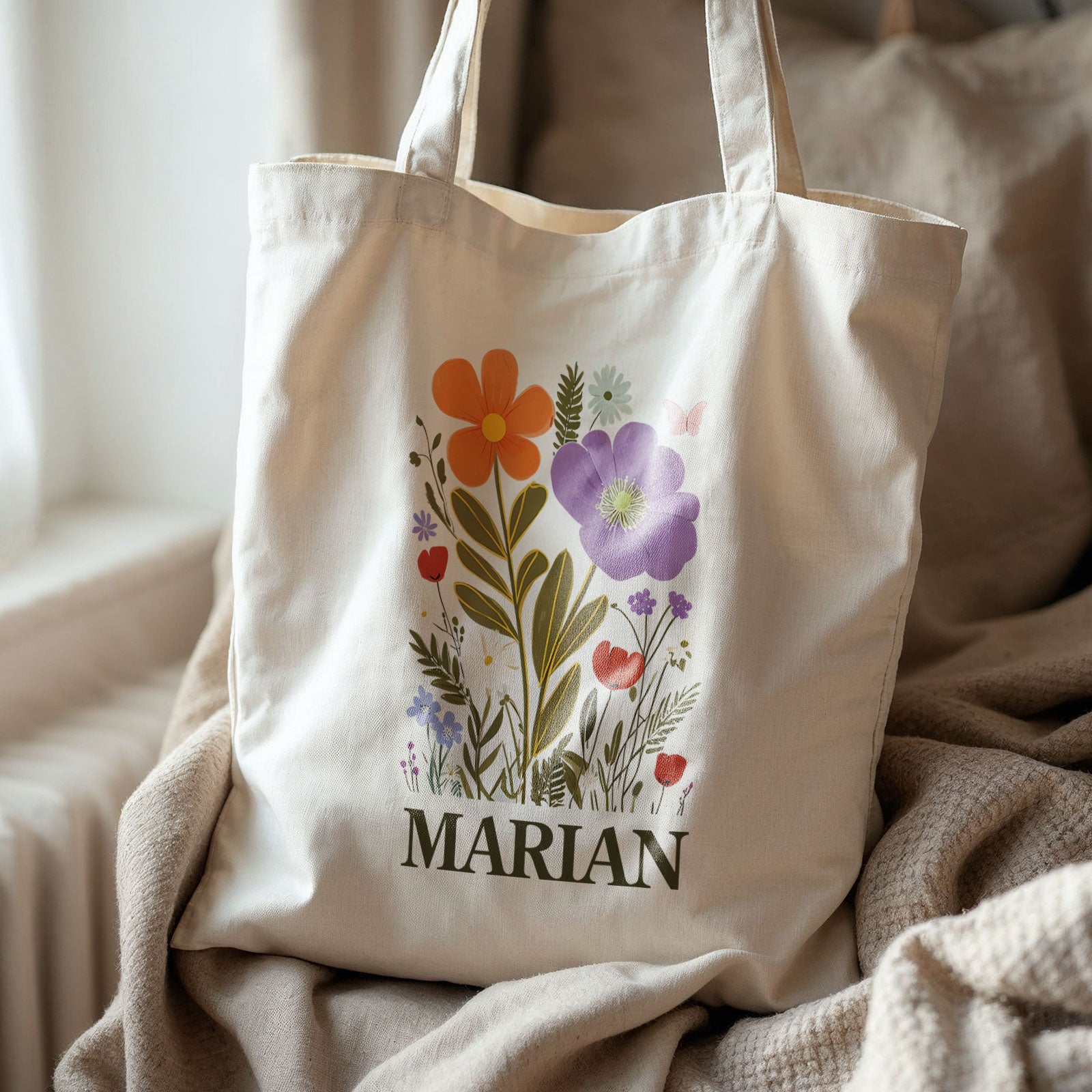 Naturelkleurige totebag met bloemenillustratie in zachte tinten en gepersonaliseerde naam in donkergroen. Botanische en boho stijl op een stoel