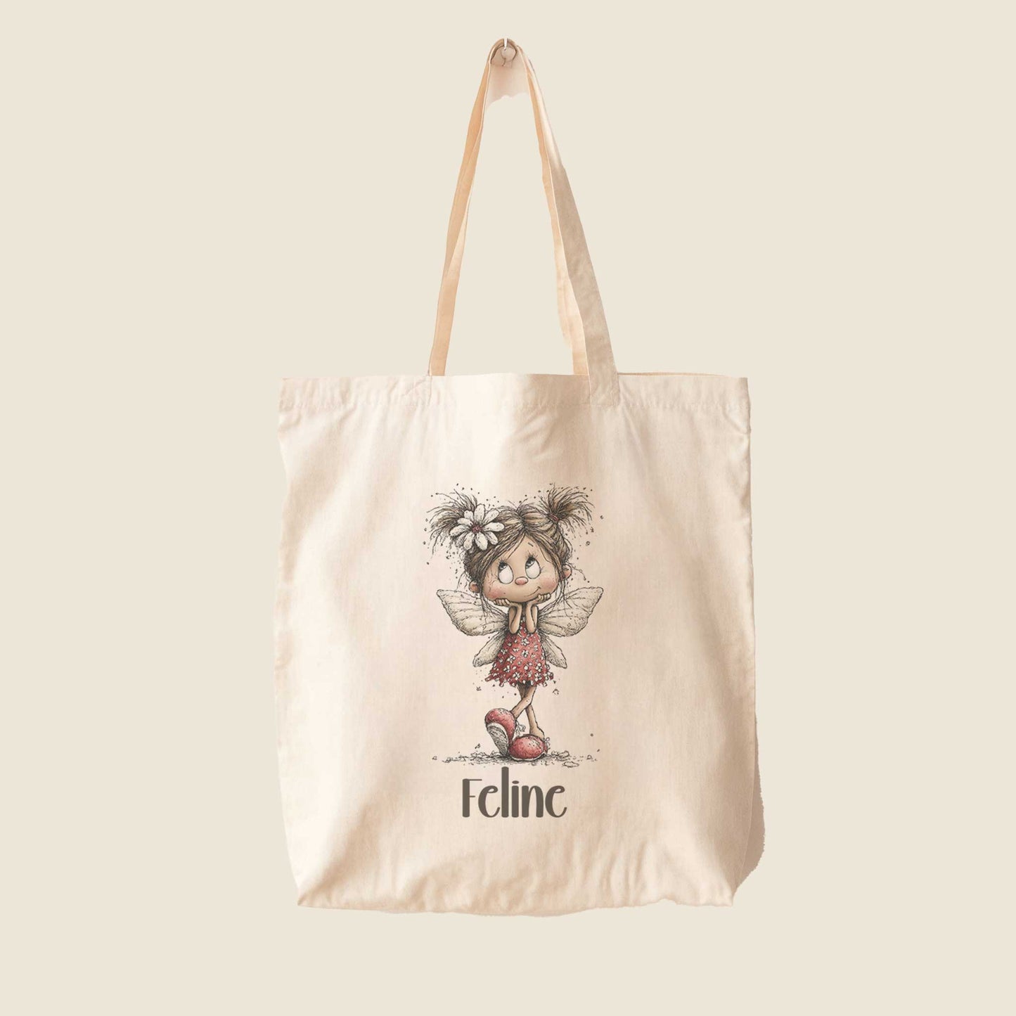 Beige totebag op een lichte achtergrond met een illustratie van een fee in een rode jurk en de naam Feline.