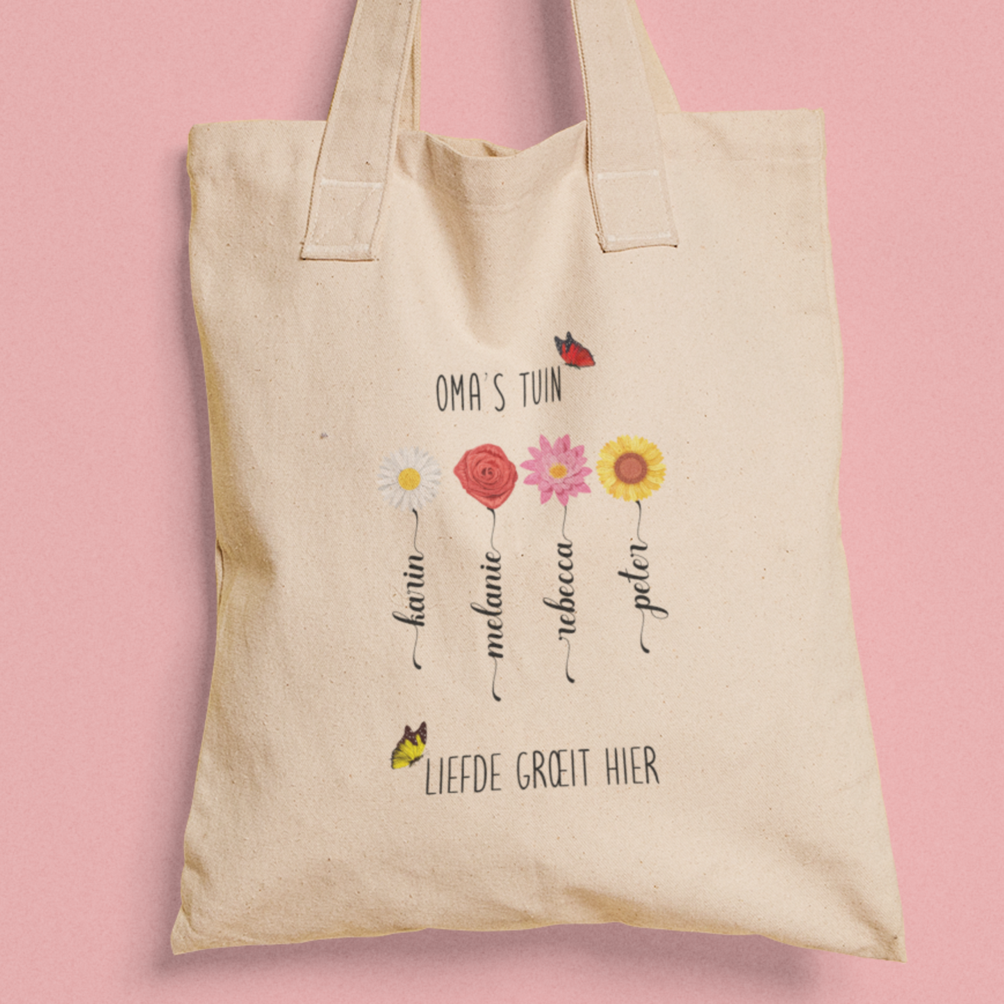 Totebag ‘Oma’s Tuin’ met vier bloemen en namen, tekst ‘Liefde groeit hier’, tegen roze achtergrond.