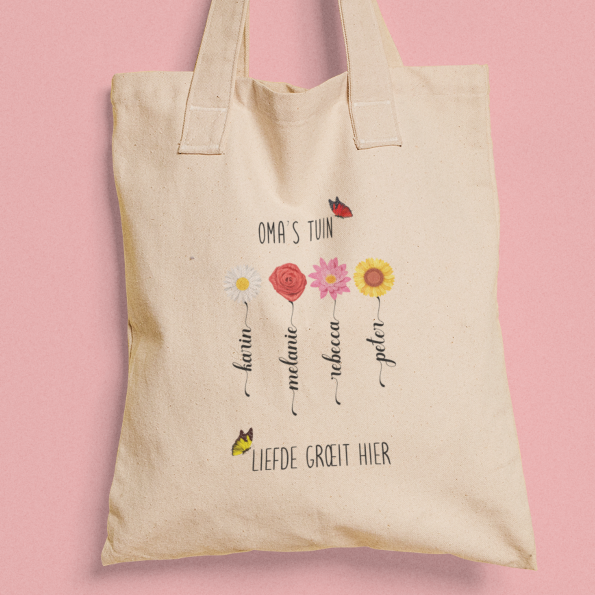 Totebag ‘Oma’s Tuin’ met vier bloemen en namen, tekst ‘Liefde groeit hier’, tegen roze achtergrond.