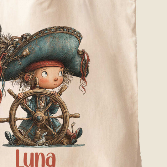 Close-up van de bedrukking op een crèmekleurige totebag met een piratenkind achter een houten stuurwiel en de naam Luna onder de illustratie.
