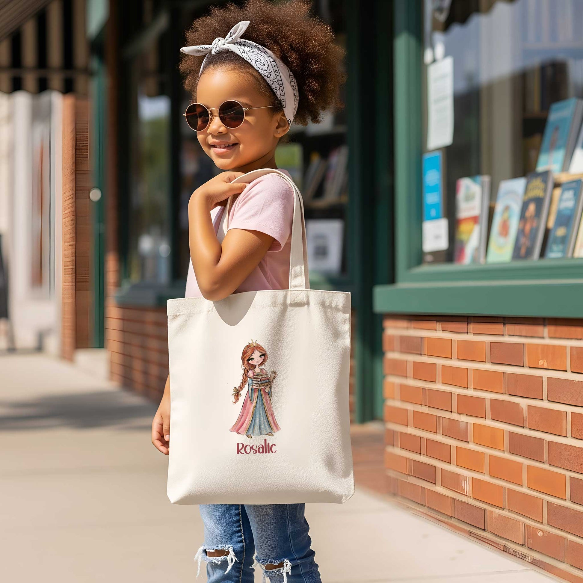 Meisje met zonnebril staat buiten voor een winkel en draagt een beige totebag over haar schouder. Op de tas staat een prinses met een stapel boeken en de naam Rosalie