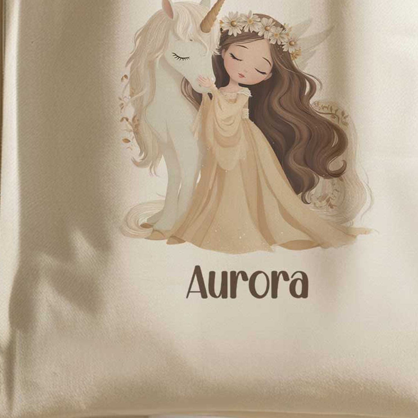 Close-up van een beige totebag met een illustratie van een prinses die een witte eenhoorn knuffelt. Onder de illustratie staat de naam Aurora.