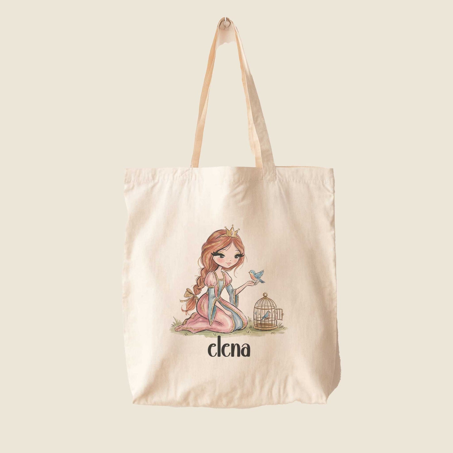 Beige totebag met een illustratie van een prinses met een blauw vogeltje op haar hand en een vogelkooitje. Onder de illustratie staat de naam Elena op een effen lichte achtergrond.