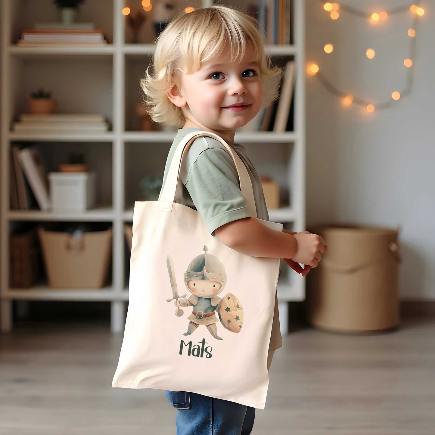 Jong kind draagt een crèmekleurige katoenen totebag met een illustratie van een ridder met zwaard en schild en de naam Mats.