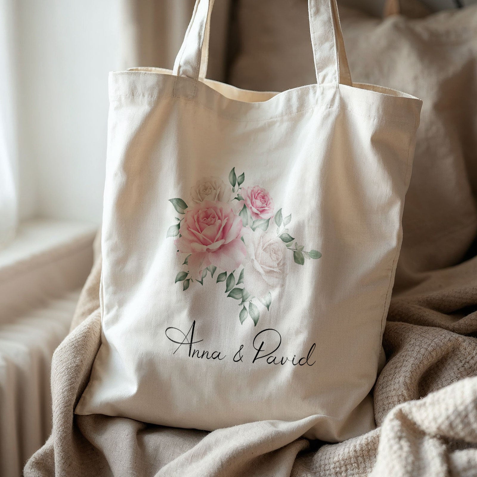 Crèmekleurige gepersonaliseerde totebag met aquarelrozen en namen Anna & David, op een beige deken in zacht daglicht