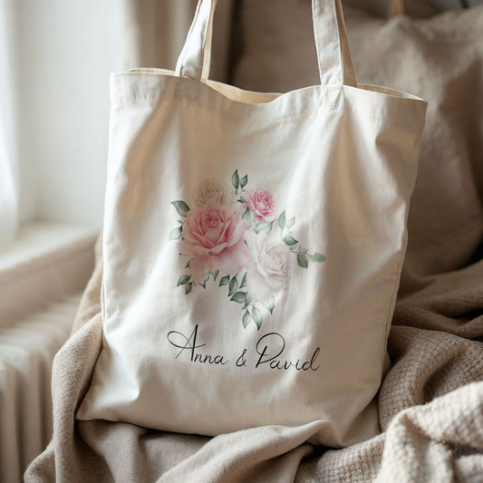Crèmekleurige gepersonaliseerde totebag met aquarelrozen en namen Anna & David, op een beige deken in zacht daglicht