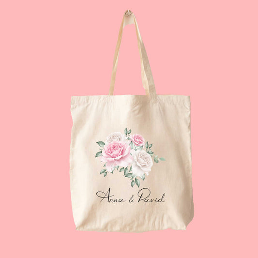Tote bag met roze en witte rozenillustratie en namen Anna & David, op effen roze achtergrond