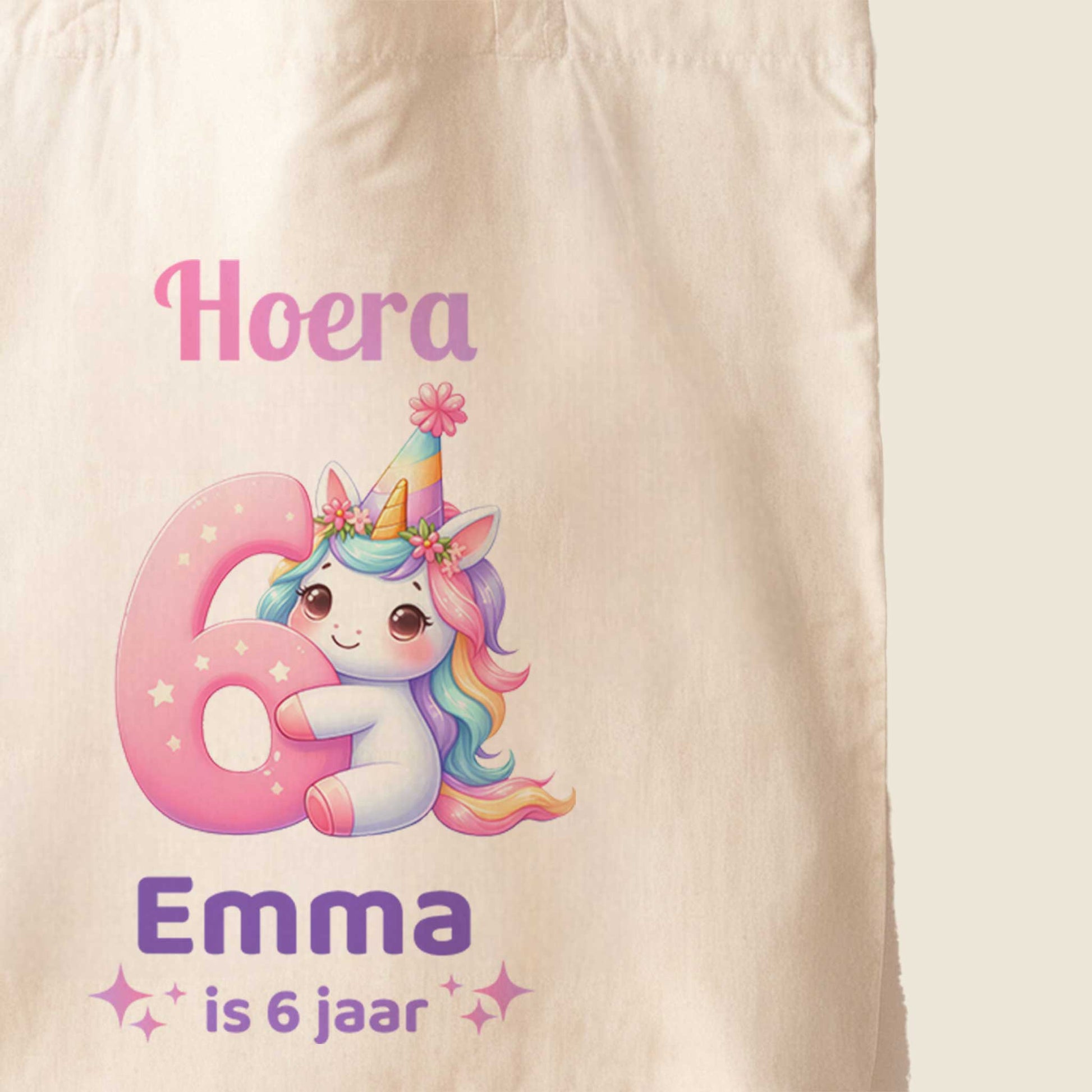 Close-up van een lichte totebag met een unicorn, een groot roze cijfer 6 en de tekst Hoera Emma is 6 jaar.