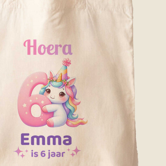 Close-up van een lichte totebag met een unicorn, een groot roze cijfer 6 en de tekst Hoera Emma is 6 jaar.