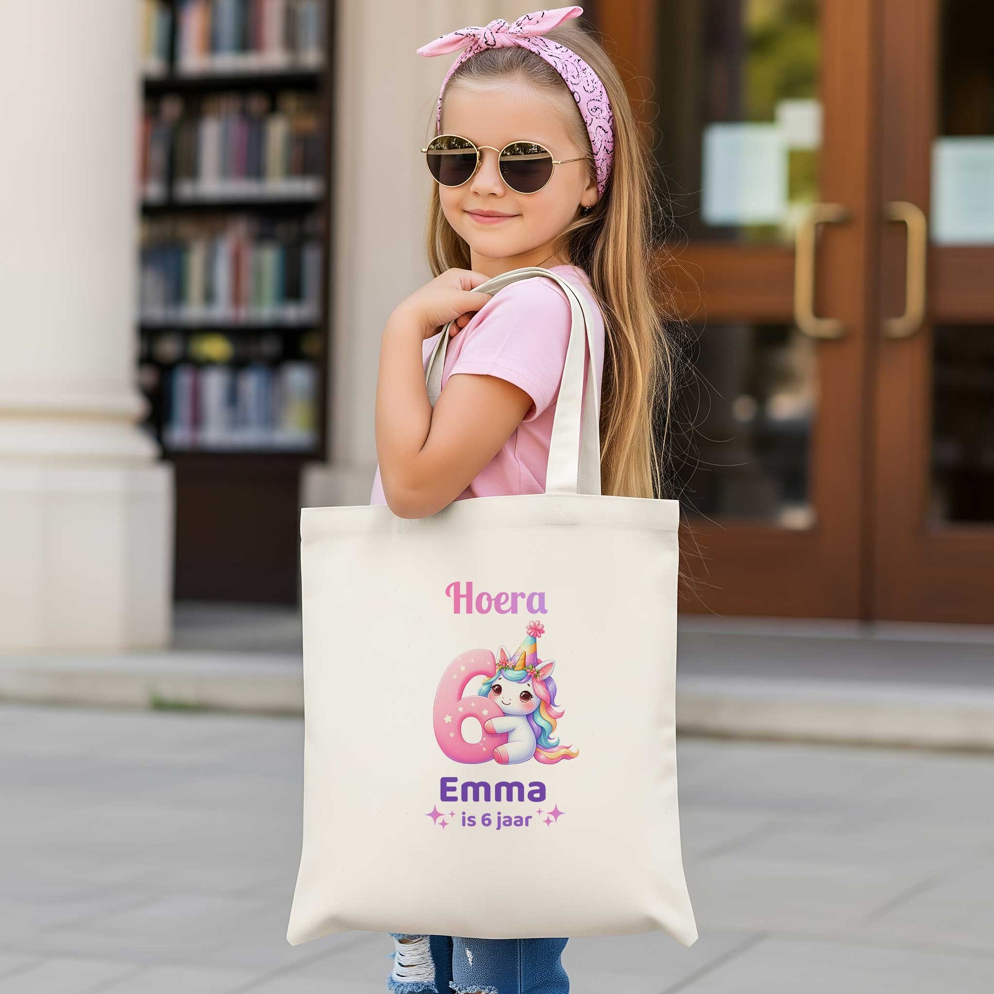 Meisje met zonnebril draagt een lichte totebag met een unicorn, een groot roze cijfer 6 en de tekst Hoera Emma is 6 jaar.
