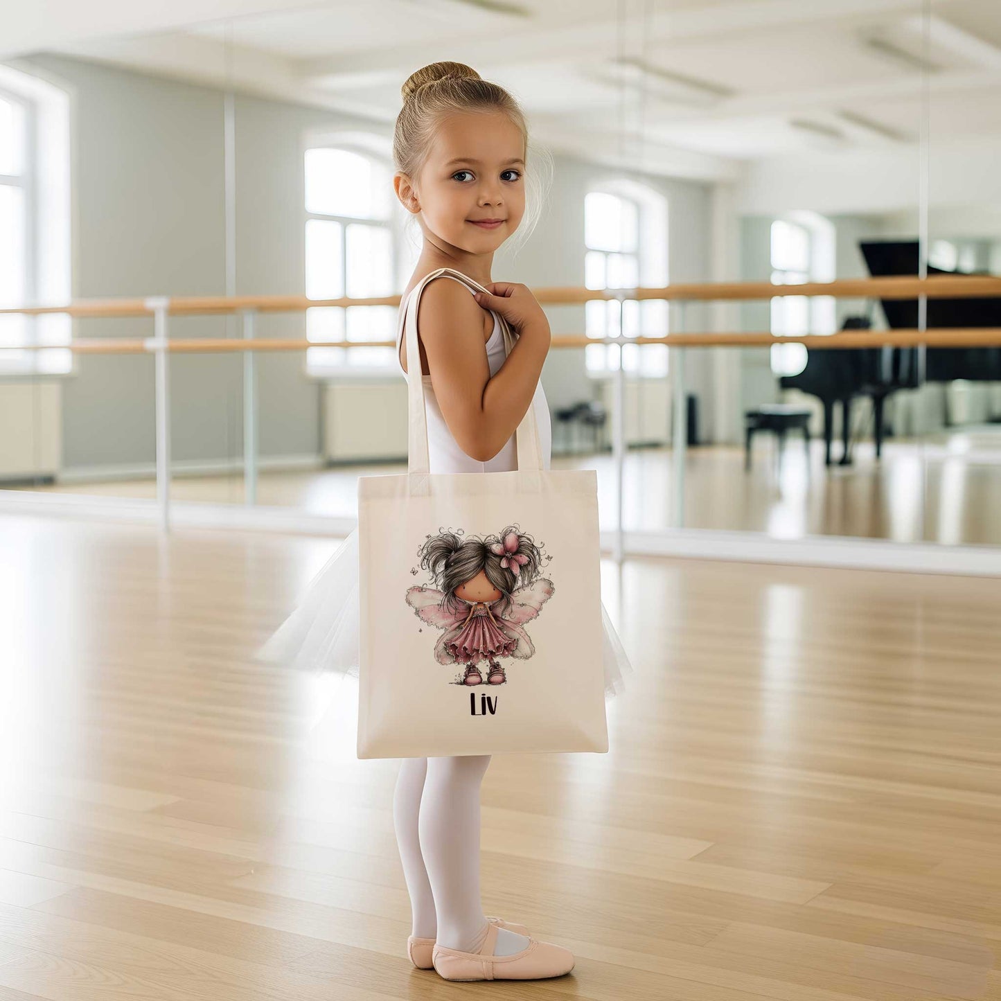Jong meisje in een balletzaal draagt een beige totebag met een fee met roze vleugels en de naam Liv.