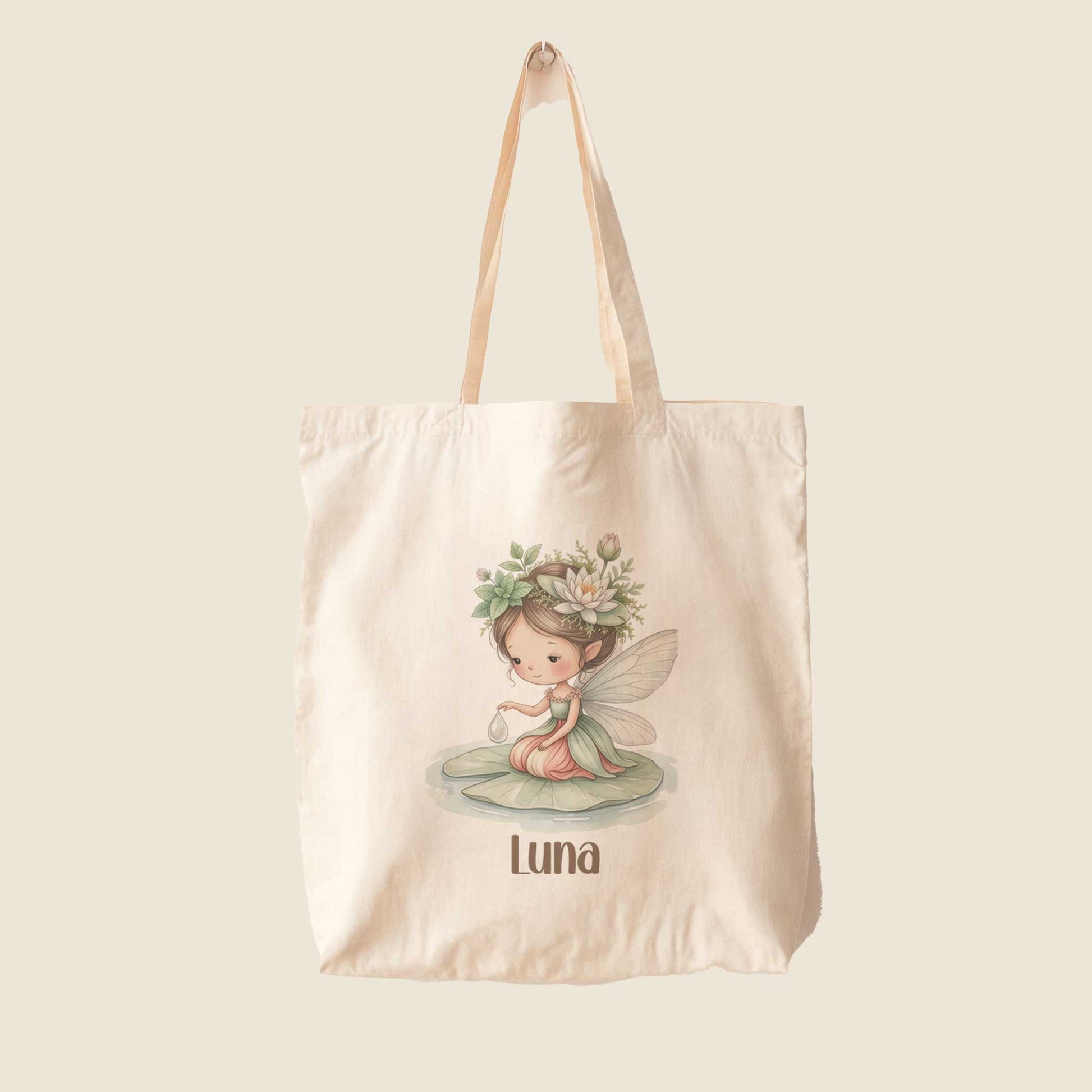 Beige totebag op een lichte achtergrond, met in het midden een illustratie van een fee op een waterlelieblad en daaronder de naam Luna.