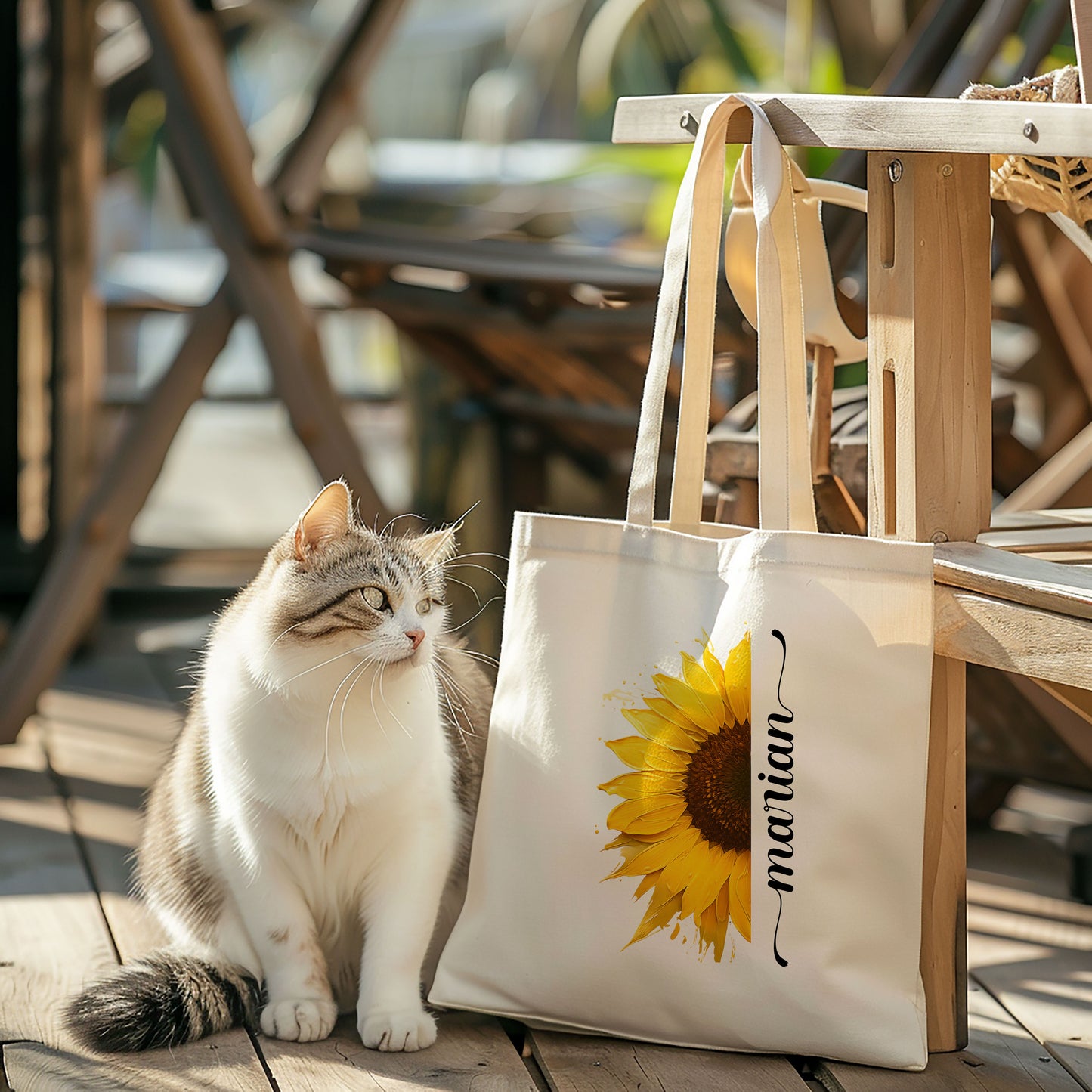 Totebag zonnebloem met naam Marian, hangend aan houten stoel, kat ernaast op houten vloer.