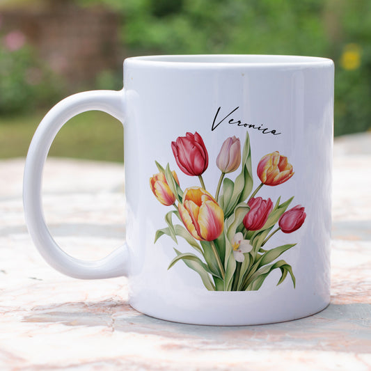 witte mok met een bos gekleurde tulpen en een personaliseerbare naam  in dun elegant zwart lettertype, mok staat op een tafel buiten.