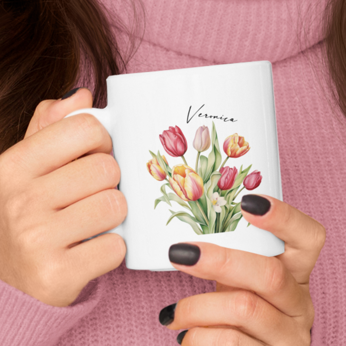 vrouw met roze coltrui die een mok vasthoudt. Haar nagels zijn zwart. Het is een witte mok met een bos gekleurde tulpen en een personaliseerbare naam  in dun elegant zwart lettertype
