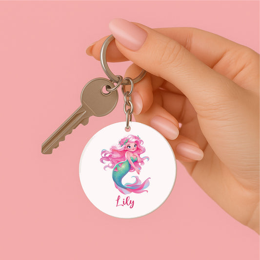 Hand met roze nagels houdt een sleutelbos vast met een gepersonaliseerde sleutelhanger waarop een zeemeermin met bloemenhaar en de naam Lily staat.
