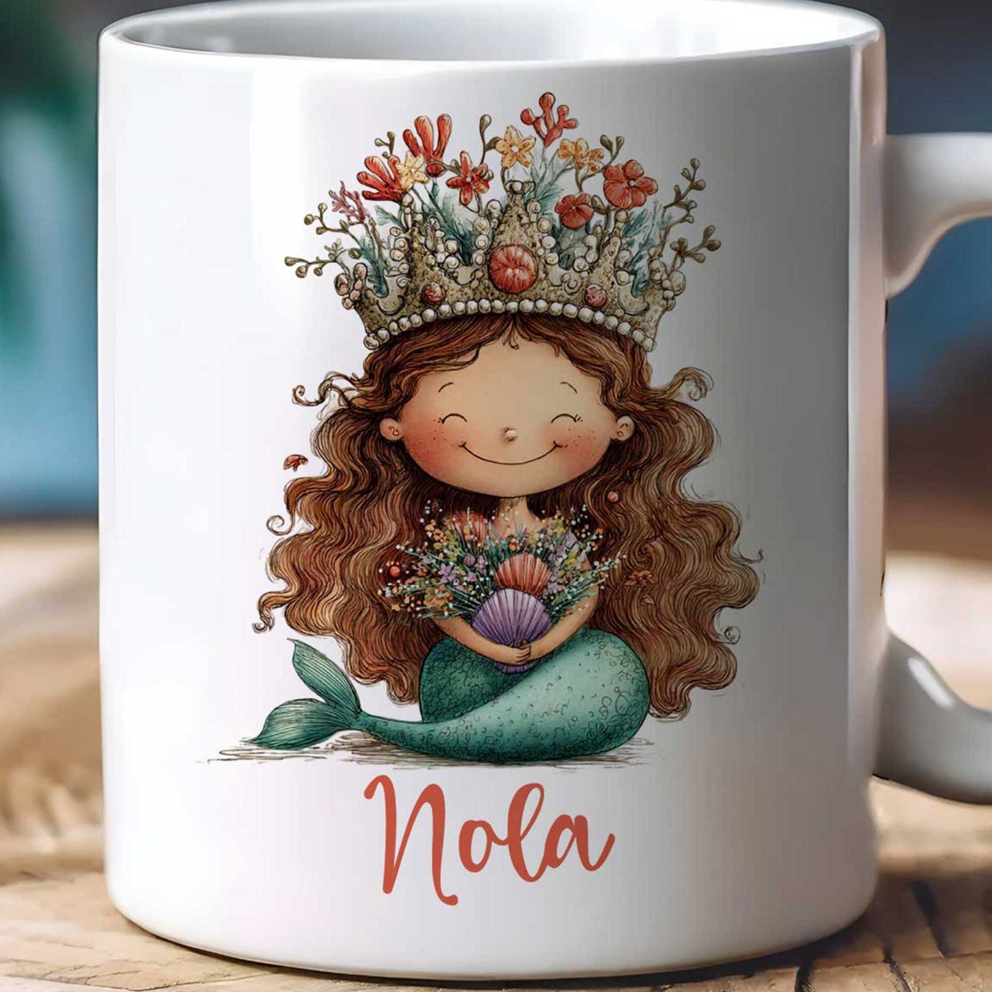 close=up van Witte mok op een beige achtergrond met een zeemeermin met koraalkroon, bloemen en schelpen in haar handen en de naam Nola onder de illustratie.