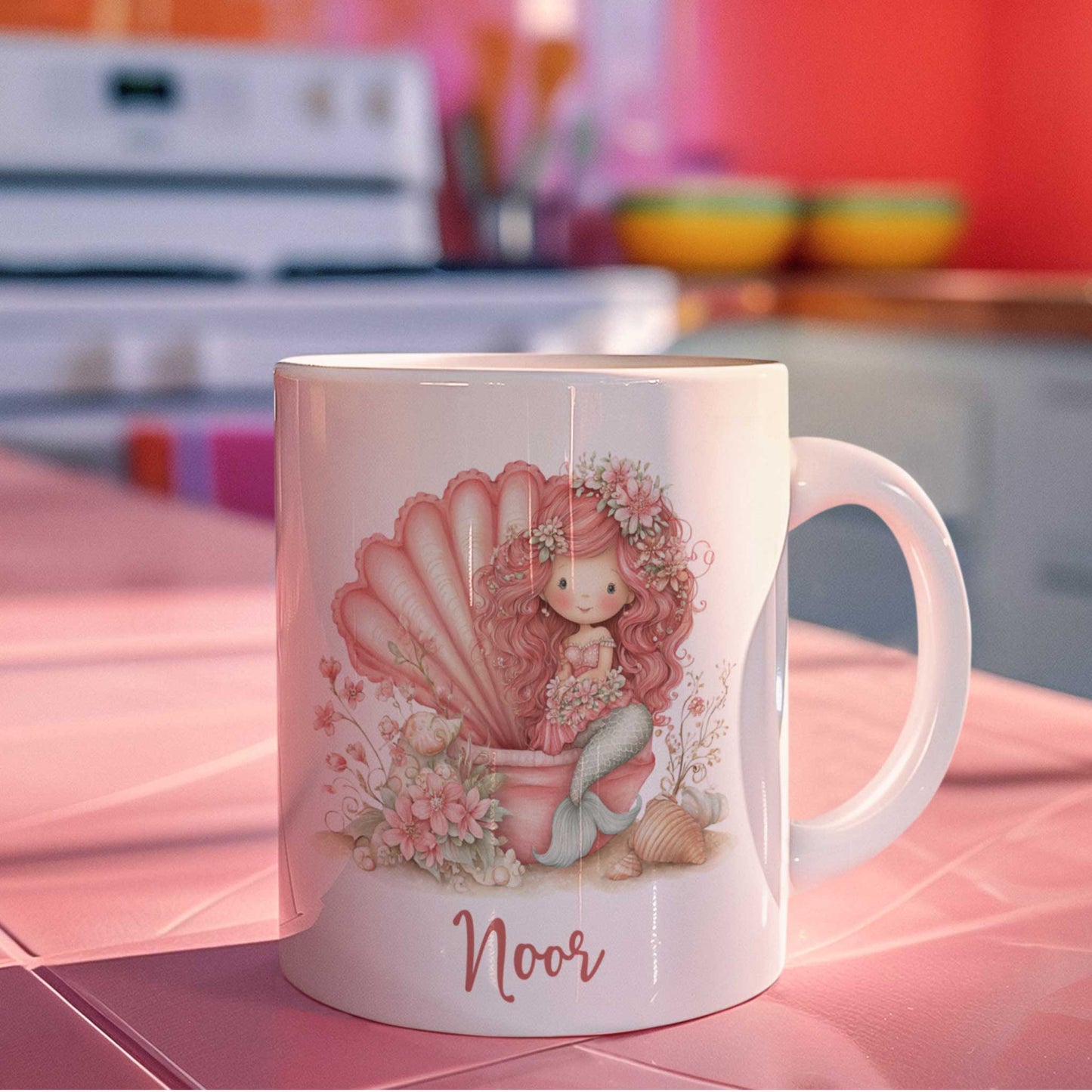 Gepersonaliseerde mok met zeemeerminillustratie op een roze keukenblad. Het ontwerp toont een roze zeemeermin in een grote schelp met bloemen, schelpen en de naam Noor onder de afbeelding.