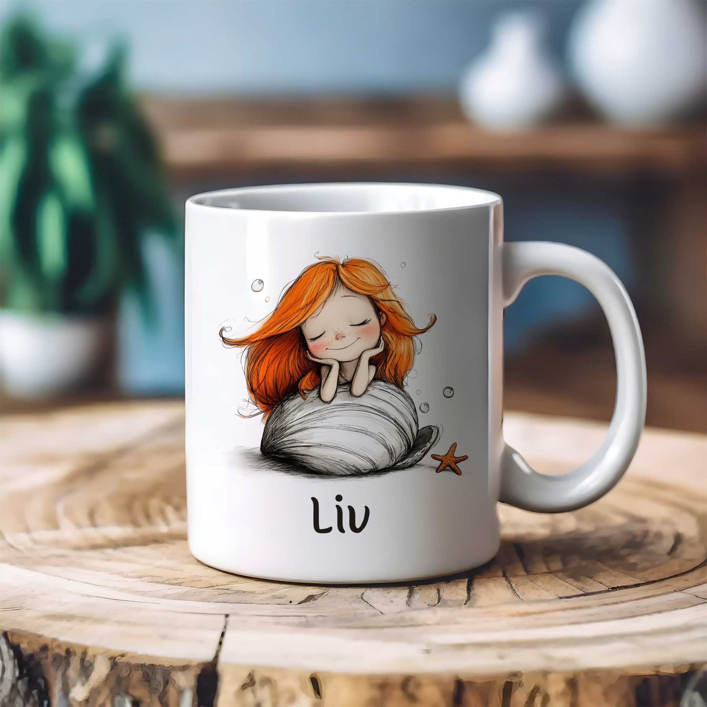 Witte keramische mok met een dromende zeemeermin met lang oranje haar op een grote witte schelp. De mok staat op een houten tafel met een onscherpe achtergrond. Onder de illustratie staat de naam Liv.