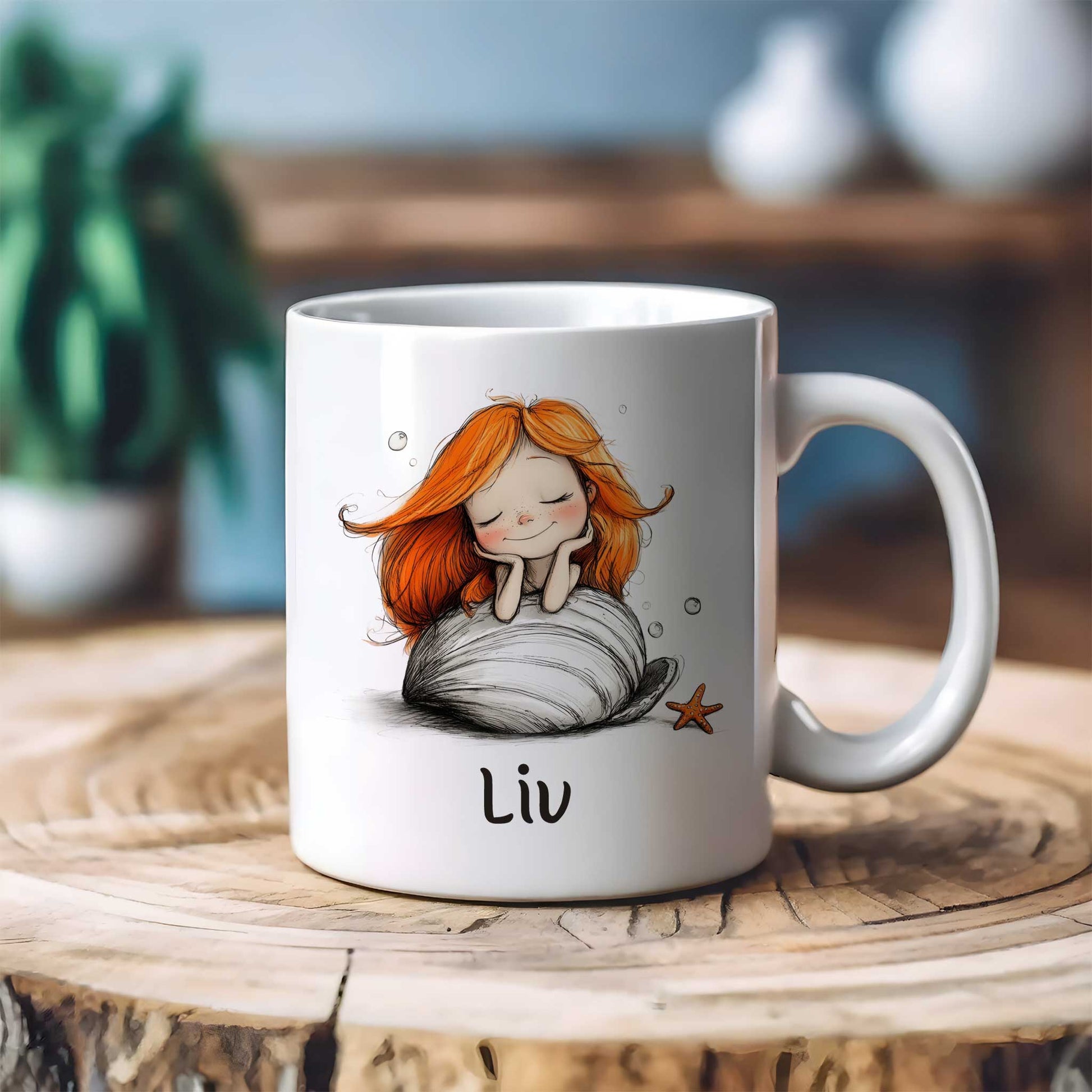 Witte keramische mok met een dromende zeemeermin met lang oranje haar op een grote witte schelp. De mok staat op een houten tafel met een onscherpe achtergrond. Onder de illustratie staat de naam Liv.