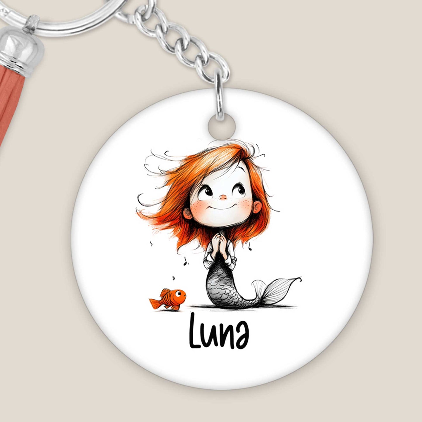 Close up van ronde sleutelhanger met zeemeerminillustratie, voorbeeldnaam Luna, metalen sleutelring en lichtbruin kwastje.