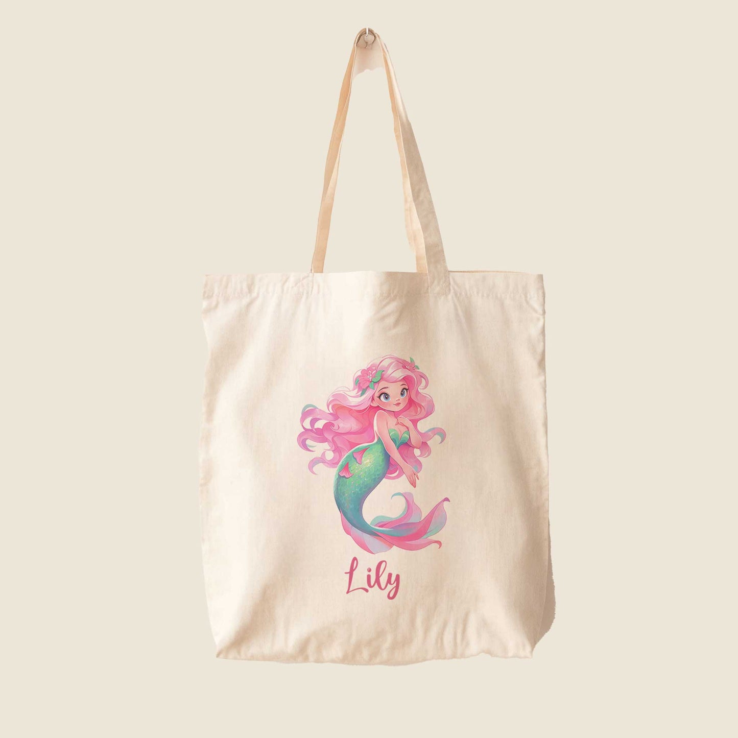 Vrijstaande katoenen totebag op een lichte achtergrond met een kleurrijke zeemeerminillustratie. De zeemeermin heeft roze haar met bloemen, een turquoise staart en de gepersonaliseerde naam Lily.