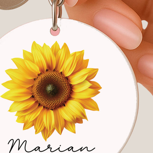 Close-up van een ronde sleutelhanger met een zonnebloem en de naam Marian.