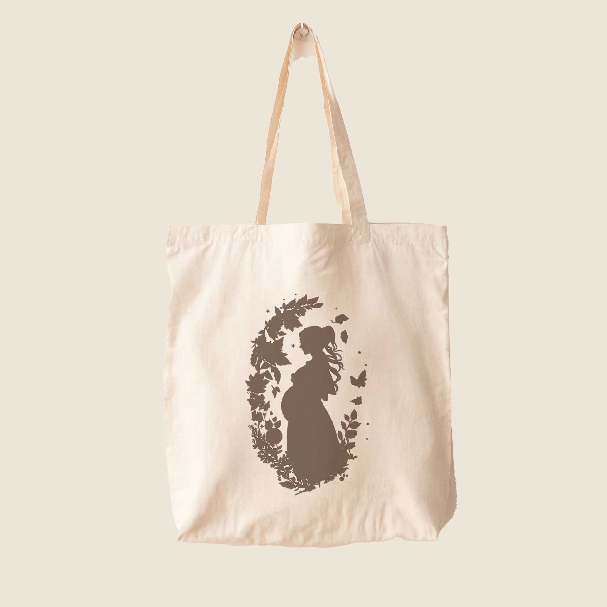 Crèmekleurige katoenen totebag met silhouet van een zwangere vrouw omringd door bloemen en vlinders op een lichte achtergrond.