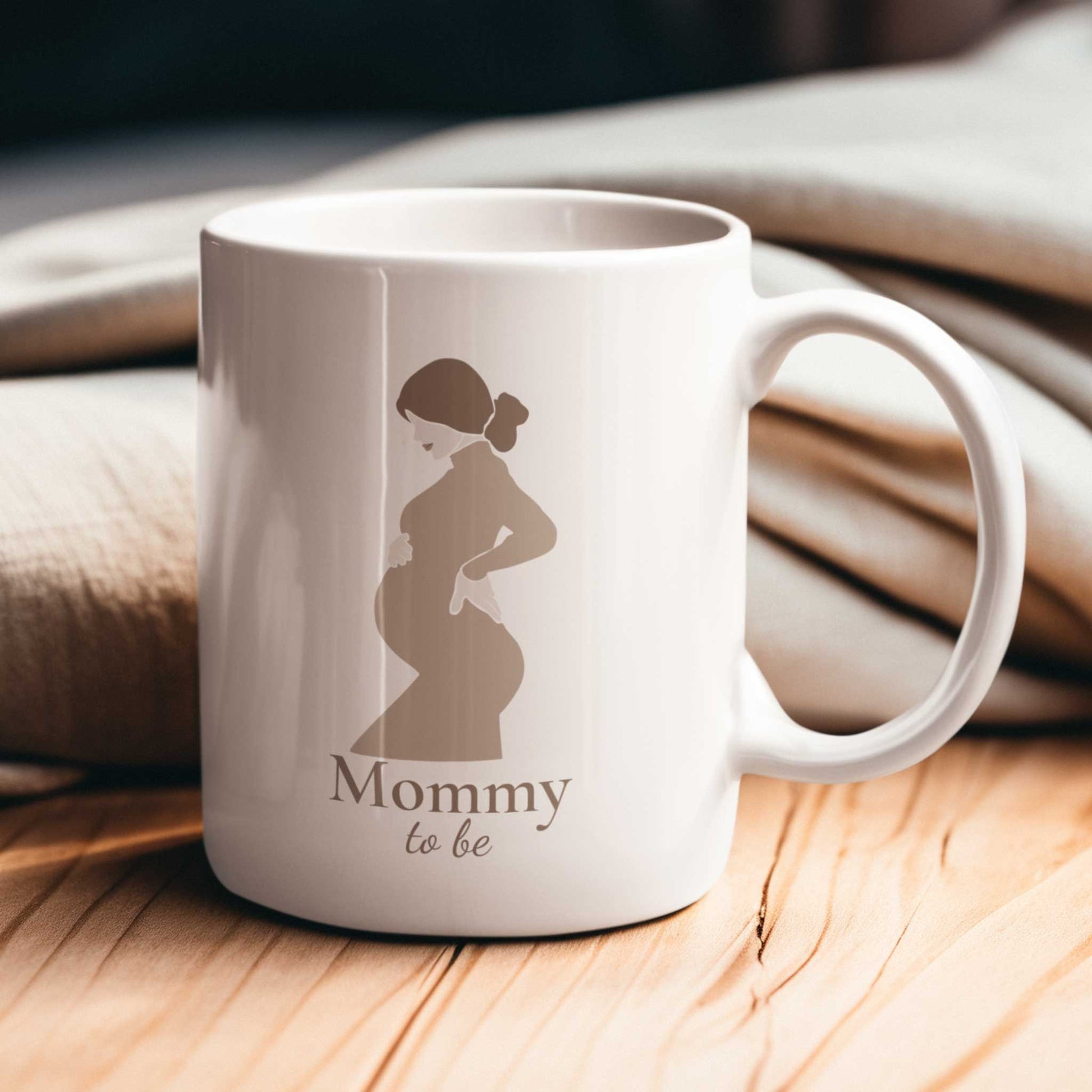 Witte zwangerschapsmok met Mommy To Be ontwerp op houten ondergrond met zachte warme sfeer en beige dekens op de achtergrond.