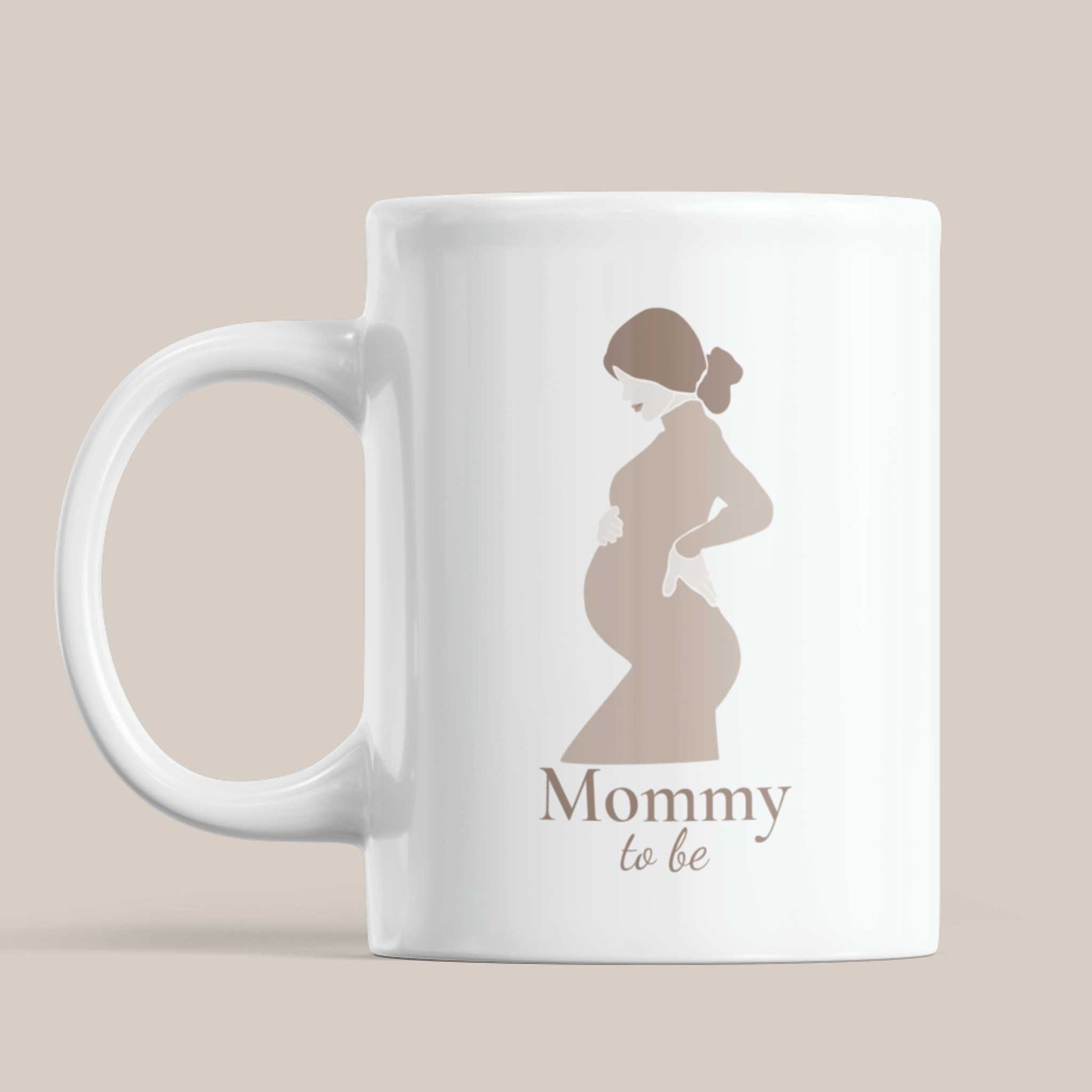 Vooraanzicht van een witte keramische Mommy To Be mok met minimalistische illustratie van een zwangere vrouw tegen een beige achtergrond.