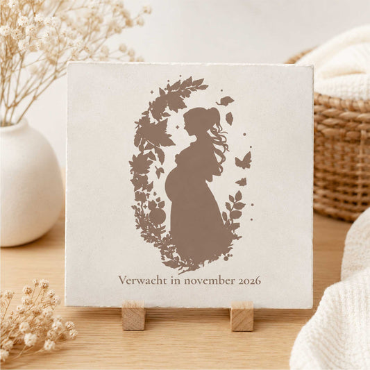 Zwangerschap tegeltje met silhouet van zwangere vrouw tussen bloemen en vlinders, geplaatst in warm boho interieur met droogbloemen.