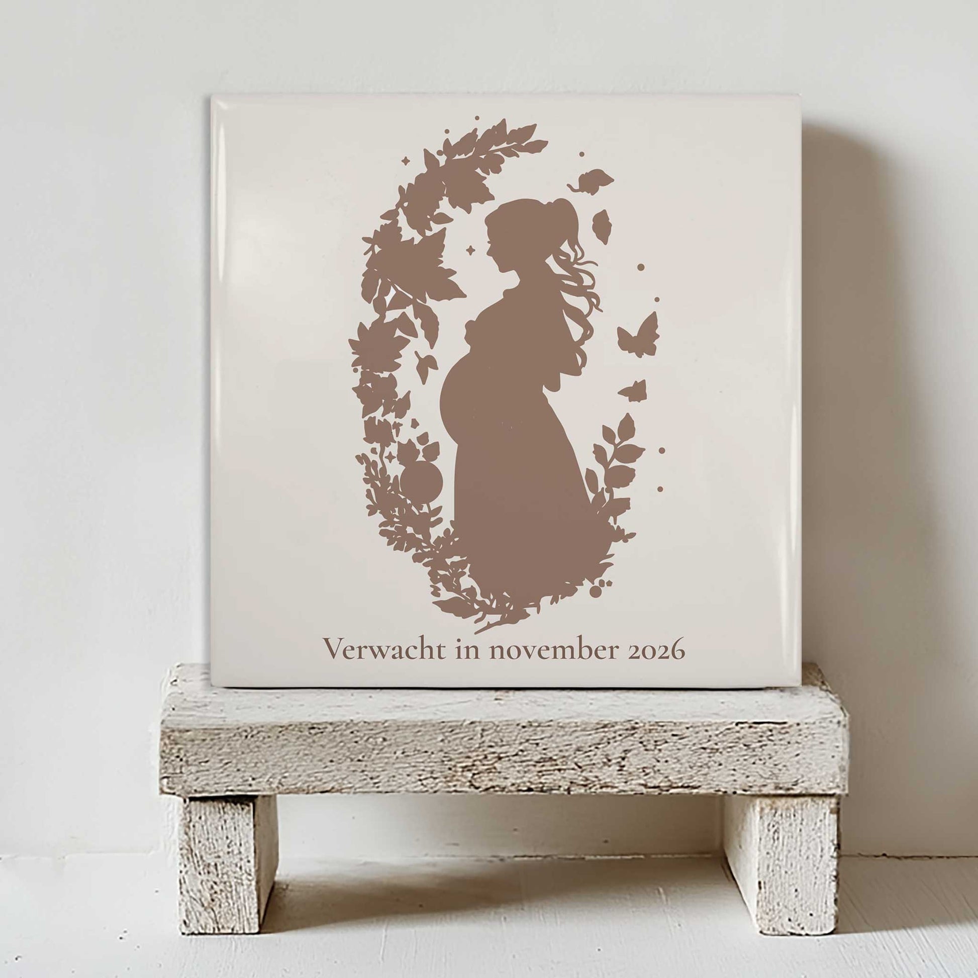 Zwangerschap tegeltje met silhouet van zwangere vrouw tussen bloemen en vlinders, geplaatst in warm boho interieur met droogbloemen.